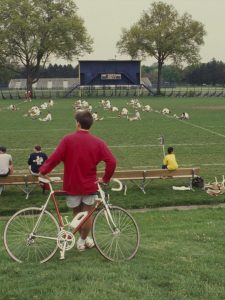 Bicyclist watches lacrosse practice.